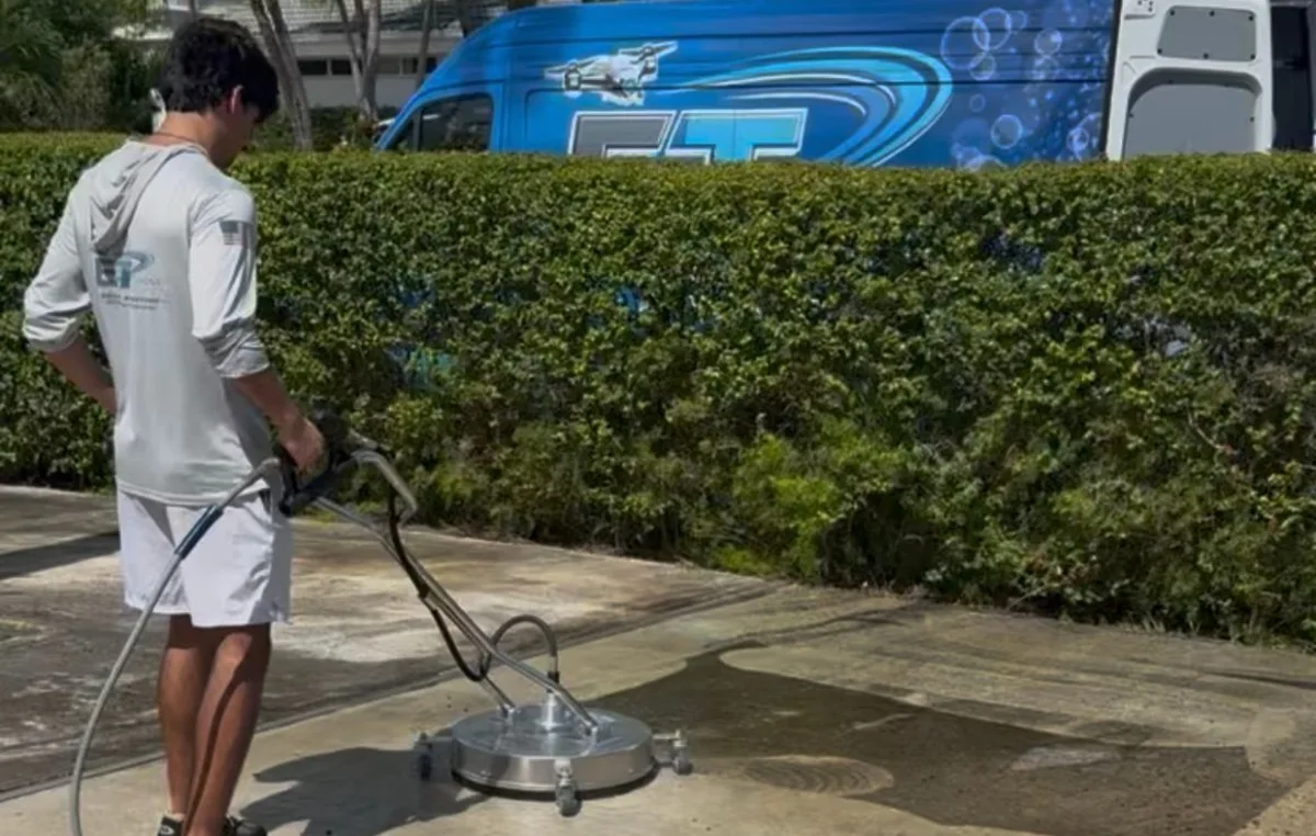 Technician pressure washing a driveway with a surface cleaner, ET van behind