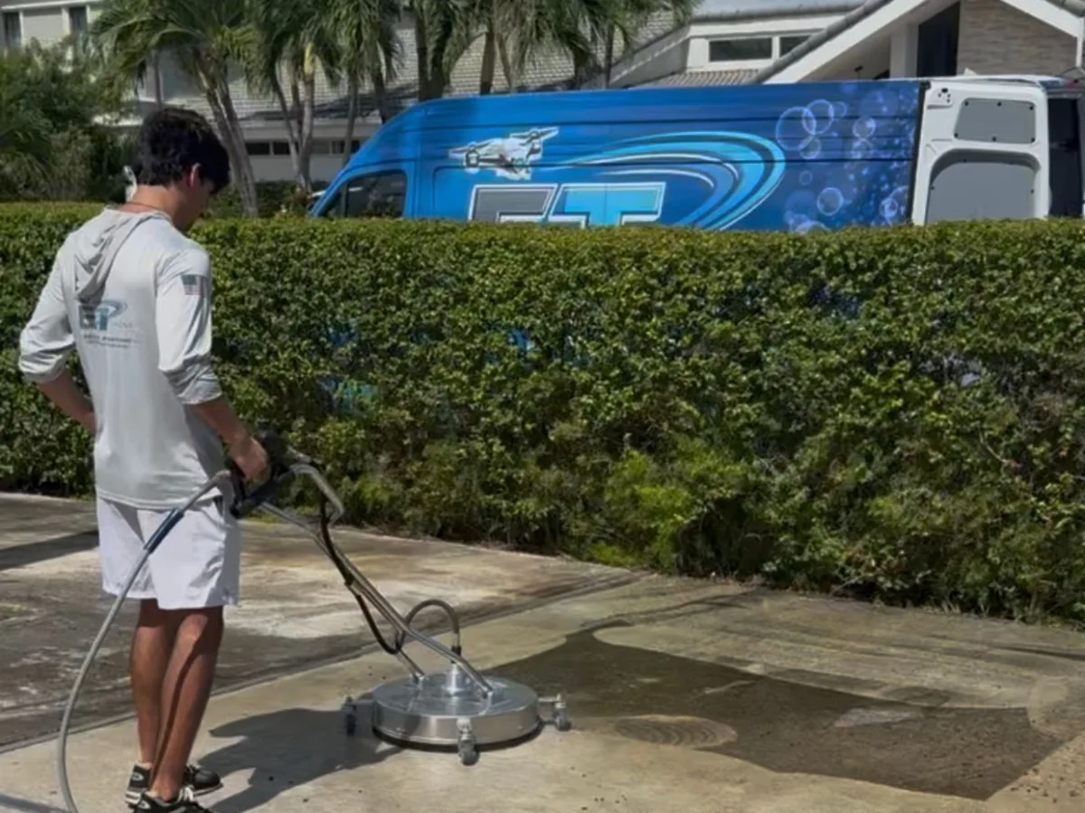 Technician pressure washing a driveway with a surface cleaner, ET van behind